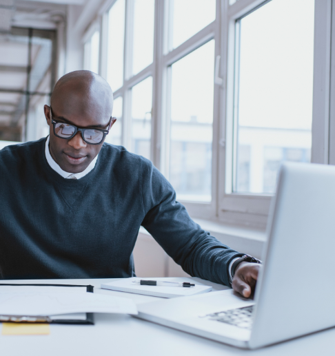 Professional man at a desk typing on a laptop while reviewing printed materials. 