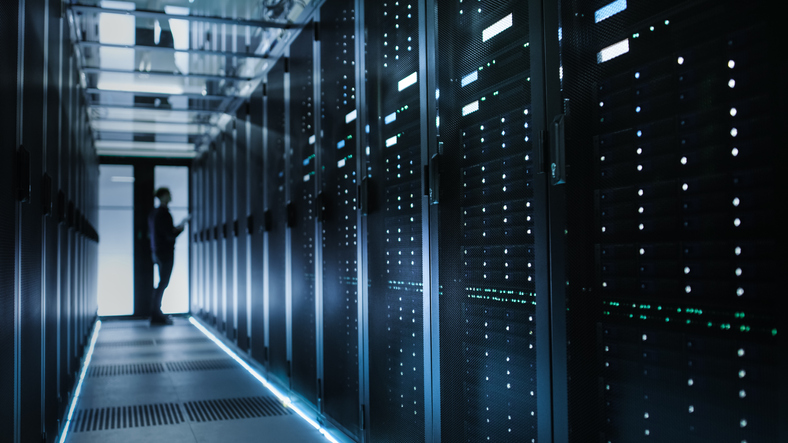 Wall of data servers with an IT technician managing the servers and checking for cyber attacks.